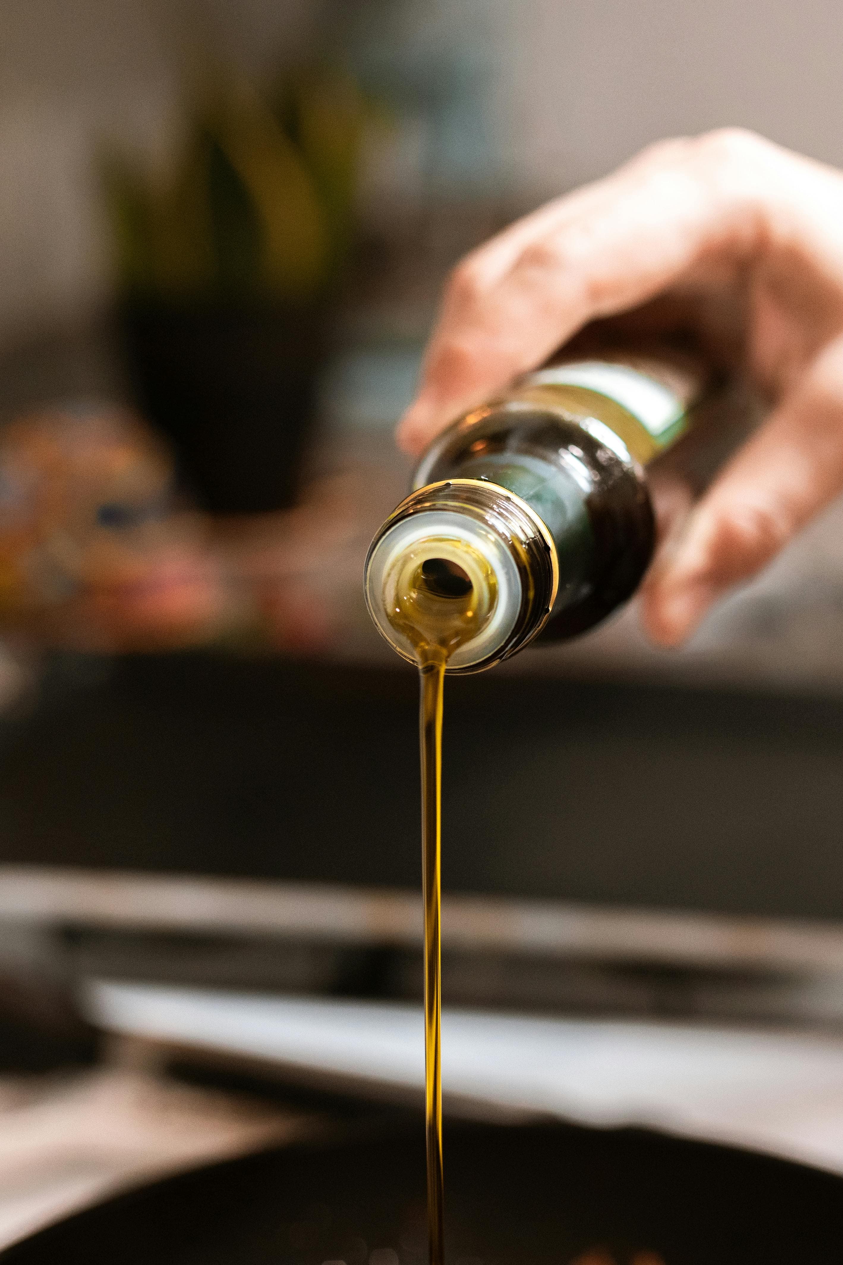 A bottle of oil being poured into a pan